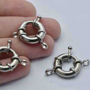 May include: Three silver-colored, round jewelry clasps. Each clasp has a circular body with a decorative, twisted wire design and a small loop for attachment. A small, ball-shaped knob is on top of each clasp.