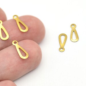 May include: Several small, gold-colored teardrop-shaped charms with a loop at the top. The charms have an open teardrop design in the center. The charms are on a white background.