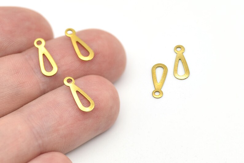May include: Several small, gold-colored teardrop-shaped charms with a loop at the top. The charms have an open teardrop design in the center. The charms are on a white background.