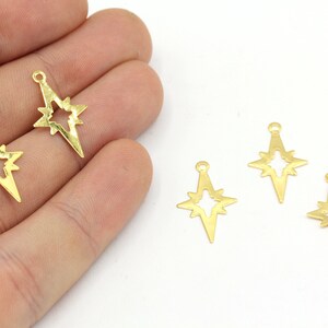Puede incluir: Varios dijes dorados en forma de estrella con un diseño de estrella recortada. Cada dije tiene un pequeño lazo en la parte superior para sujetarlo a la joyería. Los dijes se muestran sobre un fondo blanco.