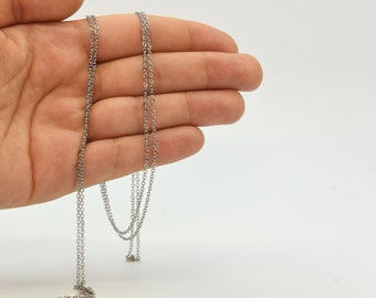 May include: A delicate silver-colored chain necklace with a fine, linked design. The necklace is displayed against a plain white background, showcasing its simple elegance. The chain is held in a hand, highlighting its length and detail.