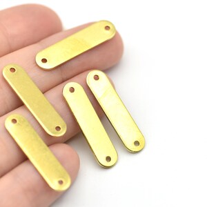 May include: Close-up of several small, rectangular brass connector bars with two holes at each end. The bars are a shiny gold color and are arranged on a white background.