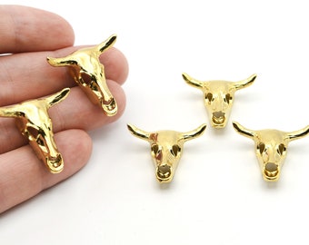 May include: Several gold-colored bull skull charms are displayed against a white background. The charms are detailed with horns and facial features. The charms are likely for jewelry making or crafting.