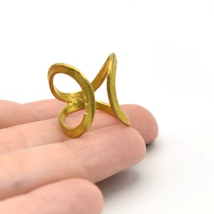 May include: A gold-colored ring with a unique, open design. The ring features a swirling, abstract shape with a loop and a vertical element. The ring is displayed against a white background.