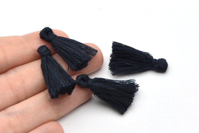 May include: Close-up of four navy blue tassels. Each tassel is made of fine, tightly-packed threads, with a looped top and a flowing, fringed bottom. The tassels are arranged against a white background.