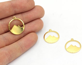 Puede incluir: Colgantes con forma de montaña dorada. Cada colgante presenta una silueta de montaña dentro de un marco circular, con un pequeño lazo en la parte superior para sujetarlo a la joyería. Los colgantes son de metal brillante.