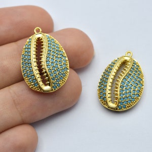 Könnte beinhalten: Zwei goldfarbene, oval geformte Anhänger. Jeder Anhänger hat ein Muscheldesign mit türkisfarbenen Steinen. Die Anhänger haben oben eine kleine Schlaufe zum Aufhängen. Der Hintergrund ist hell.