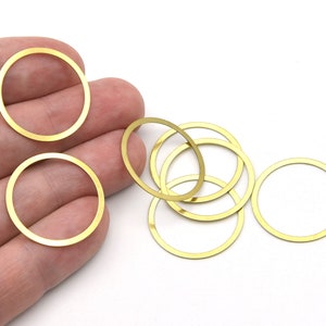 May include: A collection of small, gold-colored metal circle charms. The charms are thin and have a smooth, shiny finish. Some are round, while others are oval. They are likely used for jewelry making or other crafts.