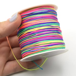 May include: A spool of colorful thread in a rainbow of hues, including pink, blue, green, and yellow. The thread is tightly wound on a white plastic spool. This thread is ideal for crafting and jewelry making.