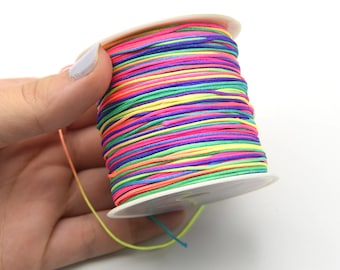 May include: A vibrant spool of thread, displaying a spectrum of colours such as pink, blue, green, and yellow. The thread is neatly wound on a white plastic reel. Suitable for various crafts and jewellery projects.