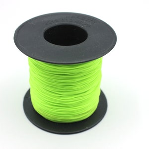 May include: A spool of bright neon green thread is tightly wound on a black plastic spool. The thread is a vibrant, eye-catching color, and the spool is set against a plain white background. The thread appears to be new and unused.