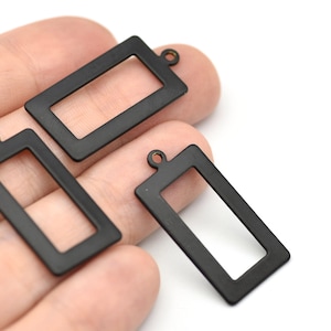 May include: Three black rectangular metal charms with a small loop at the top for attaching to jewelry. The charms have a matte finish and a hollow center. The charms are shown against a white background.
