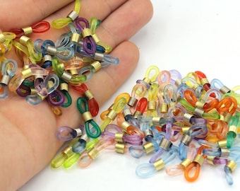 May include: A collection of colorful eyeglass holders in various shades, including red, orange, yellow, green, blue, and purple. Each holder features a clear loop and a gold-colored metal connector. The holders are designed to secure eyeglasses.