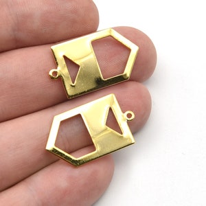 Könnte beinhalten: Zwei goldfarbene geometrische Anhänger. Jeder Anhänger hat eine rechteckige Form mit einem ausgeschnittenen Fünfeck und einem Dreieck. Oben befindet sich eine kleine Schlaufe zum Befestigen an Schmuck. Die Anhänger werden auf weißem Hintergrund gezeigt.