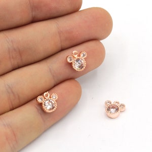 May include: Rose gold-colored charms in the shape of a mouse head, each with a clear, round center stone and three smaller stones for the ears. The charms are small, delicate, and suitable for jewelry making.