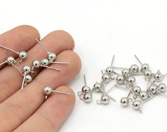 May include: A collection of silver-colored earring posts with a small, round ball at the top and a straight post extending from the ball. The earrings are scattered on a white surface.