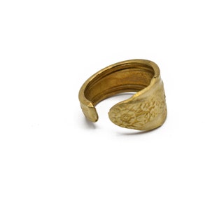 May include: A handcrafted brass ring with a floral design on the face. The adjustable ring is made from a repurposed spoon, showcasing a unique, vintage aesthetic. The ring is a warm gold color.