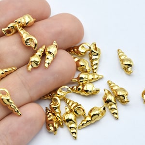 May include: A collection of small, shiny gold-colored seashell charms. These miniature, detailed conch shell pendants are ideal for jewelry making or craft projects. The charms are displayed against a neutral background.