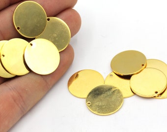 May include: A collection of shiny, gold-colored, round metal charms with a small hole near the edge. The charms are arranged in a cluster, with some overlapping. The surface of the charms reflects light, creating a bright, polished appearance. These are likely used for jewelry making or crafting.