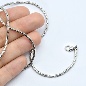Op de afbeelding: Een zilverkleurige ketting met een uniek, gesegmenteerd ontwerp. De ketting heeft een karabijnsluiting en een kleine lus aan het andere uiteinde. De ketting wordt gepresenteerd tegen een witte achtergrond.
