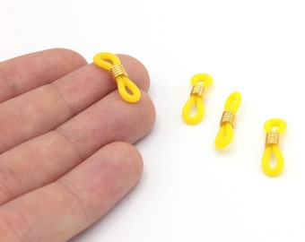 May include: Yellow eyeglass retainers with gold-colored metal accents. The retainers are made of a flexible material and are designed to secure eyeglasses. Several retainers are visible against a white background.