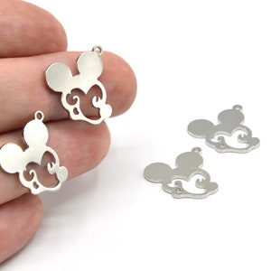 May include: Silver-colored metal charms in the shape of a mouse head with decorative swirls. The charms have a small loop at the top for attaching to jewelry or other crafts. Several charms are visible against a white background.