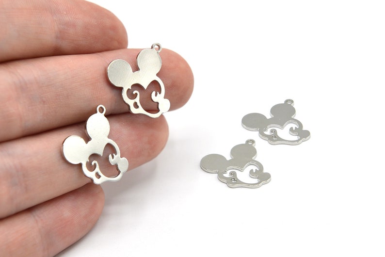 May include: Silver-colored metal charms in the shape of a mouse head with decorative swirls. The charms have a small loop at the top for attaching to jewelry or other crafts. Several charms are visible against a white background.