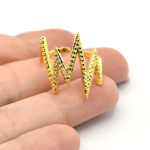 以下が含まれることがあります： 心拍数または音波に似た、ジグザグのデザインのゴールドカラーのリング。 リングはテクスチャ加工された表面を持ち、白い背景に表示されています。 このリングのデザインは、ユニークで人目を引くジュエリーです。