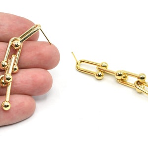 May include: Gold-colored chain link earrings. Each earring features a series of connected U-shaped links with small, round accents. The earrings are displayed against a white background, highlighting their shiny, metallic finish.