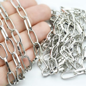 May include: Close-up of a silver chain with elongated oval links. The chain is displayed against a white background. The links are connected in a repeating pattern, creating a continuous strand. The chain is likely used for jewellery or crafting.