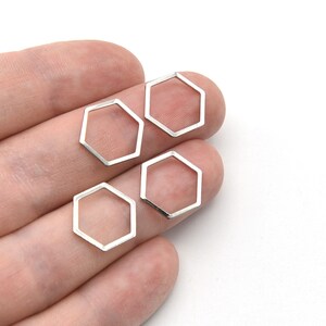 May include: Four silver-coloured, open-frame hexagon charms. The charms are displayed against a neutral background. These geometric charms are suitable for jewellery making and other craft projects.