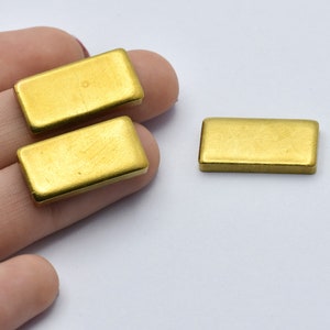 May include: Three rectangular, gold-colored metal beads are displayed against a white background. The beads have a brushed texture and a slightly rounded shape. The beads are likely used for jewelry making or other craft projects.