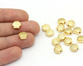 May include: A collection of small, gold-colored seashell beads. Each bead has a detailed shell design and a small hole for stringing. The beads are scattered on a white surface, with some held in a hand.