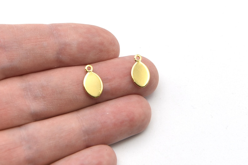 May include: Two small, gold-colored oval charms with a loop at the top for attaching to jewelry. The charms are smooth and shiny, with a simple, elegant design. Perfect for earrings or pendants.