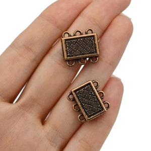 May include: Two bronze-colored rectangular jewelry clasps with a woven pattern. Each clasp has three loops on each end for attaching to jewelry pieces. The clasps are held in a hand against a white background.