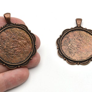 May include: Two antique bronze-colored pendant trays with scalloped edges and a textured surface. Each pendant has a loop at the top for a chain. The trays are round and have a decorative border.