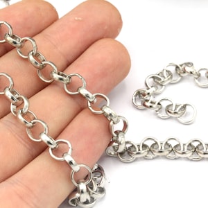 May include: A silver-colored chain necklace with a series of interconnected circular links. The chain is displayed against a neutral background, highlighting its metallic sheen and design. The necklace is a classic jewelry piece.