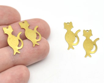 Puede incluir: Cuatro pequeños dijes dorados con forma de gato. Cada dije tiene un agujero en la parte superior para ensartar y una silueta de gato estilizada con cola curva y pata levantada. Los dijes están sobre un fondo blanco.