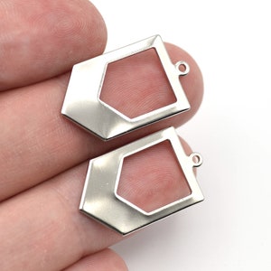 May include: Two silver-colored geometric charms with a hexagonal cutout and a small loop at the top for attaching to jewelry. The charms have a shiny, reflective surface and are displayed against a white background.