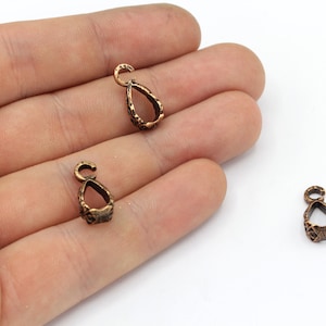 Op de afbeelding: Close-up van verschillende kleine, bronskleurige hangerbeugels. Elke beugel heeft een druppelvorm met een getextureerd oppervlak en een kleine lus aan de bovenkant om aan een ketting of ander sieradenonderdeel te bevestigen.