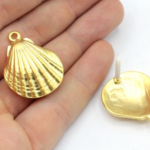 May include: Two gold-colored seashell-shaped earring components. One is a pendant with a loop, and the other has a post for piercing. The earrings have a textured, ridged surface.