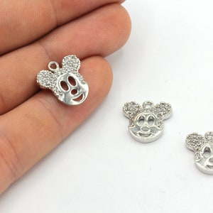 May include: Silver-colored Mickey Mouse charm pendants. The charms feature a Mickey Mouse face design with rhinestone accents on the ears. The charms have a small loop at the top for attaching to jewelry.