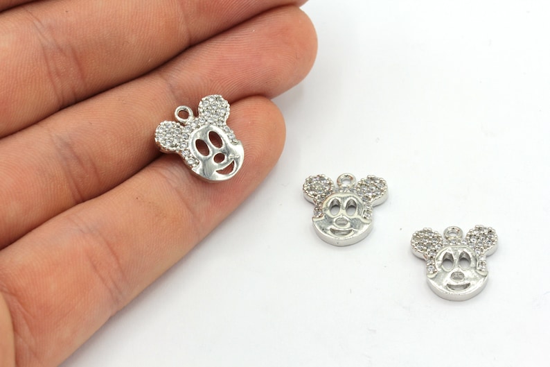 May include: Silver-colored Mickey Mouse charm pendants. The charms feature a Mickey Mouse face design with rhinestone accents on the ears. The charms have a small loop at the top for attaching to jewelry.