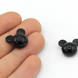 May include: Two glossy black Mickey Mouse-shaped beads. The beads have a round head with two smaller circular ears. The beads are on a white background.