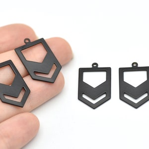 May include: Black metal geometric pendant charms with a rectangular shape and a chevron design. These charms have a small loop at the top for attaching to jewelry. The charms are shown against a white background.