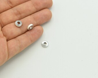 May include: Close-up of several small, silver-colored metal beads with a hole in the center. The beads are round and have a flat, disc-like shape. The beads are on a white background.