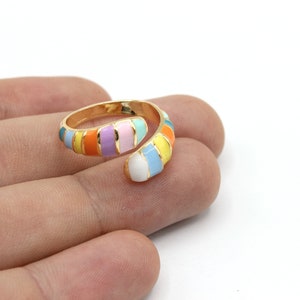 May include: A gold-toned, adjustable ring with a colorful enamel design. The ring features a spiral design with alternating stripes of orange, yellow, purple, pink, blue, and white enamel. The ring is shown on a hand.