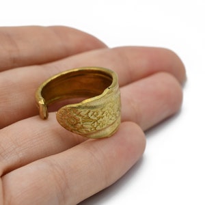 May include: A gold-colored adjustable ring with a floral design. The ring is made of metal and has an open design. The floral pattern is embossed on the front of the ring.