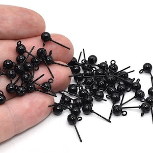 May include: A collection of small, black metal charms. Each charm features a round bead, a straight post, and a small loop. The charms are scattered against a white background, suggesting a craft or jewelry-making theme.