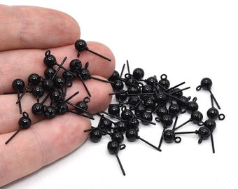 May include: A collection of small, black metal charms. Each charm features a round bead, a straight post, and a small loop. The charms are scattered against a white background, suggesting a craft or jewelry-making theme.